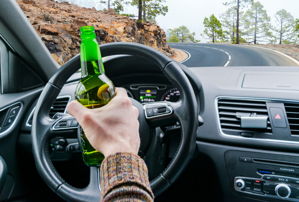 man driving while holding an alcohol bottle