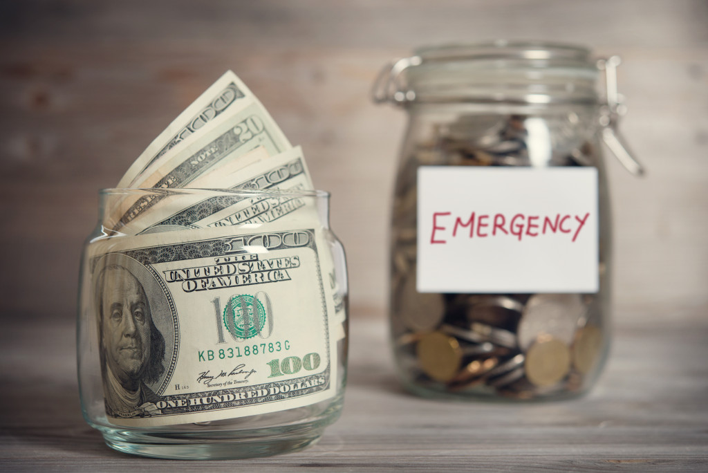 dollars inside a jar while coins are inside a jar with an emergency fund tag