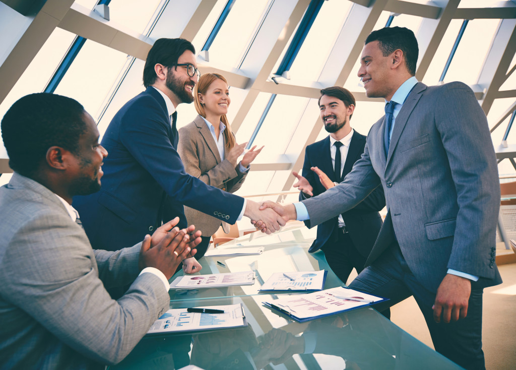 two professionals shaking hands and people clapping at the background