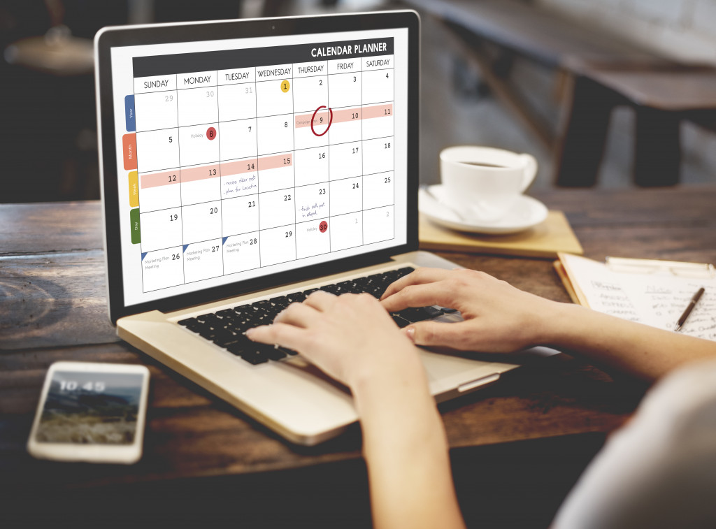 A person typing texts on a calendar planner on a laptop in a cafe