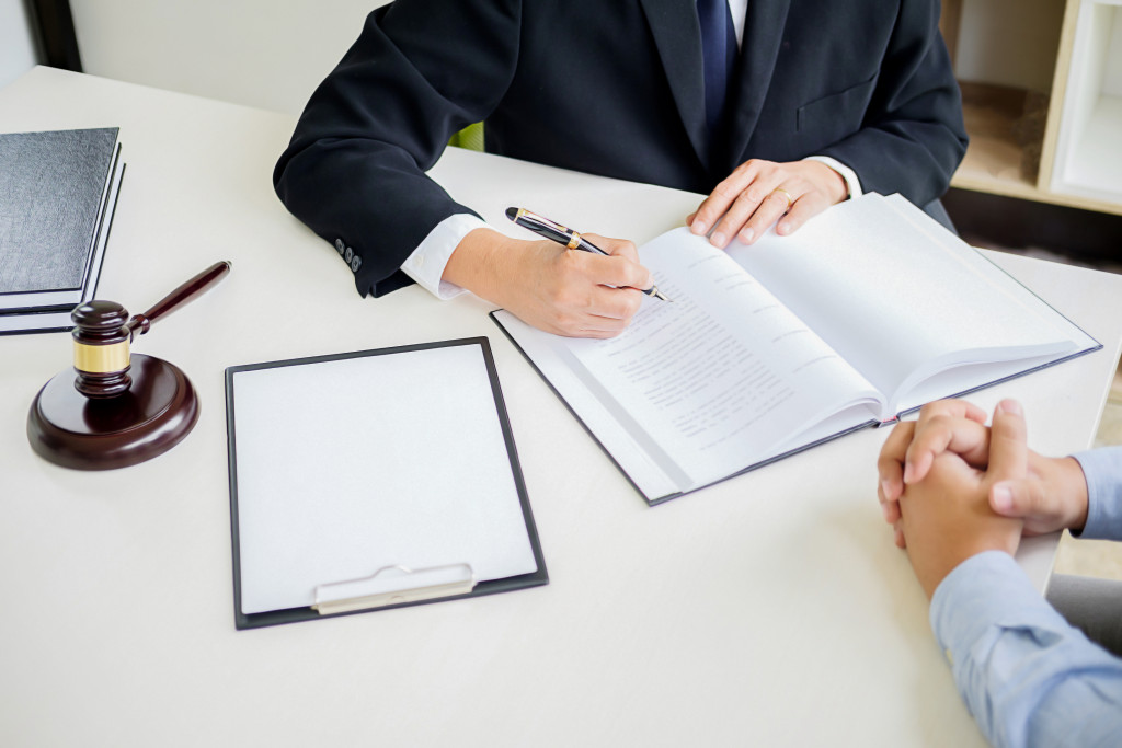 Man in business suit taking down notes on a table with a gavel and a clipboard and talking with another man