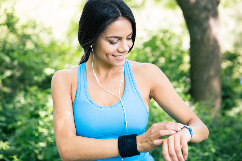 Smiling woman wearing sports t shirt using smart watch outdoors in park