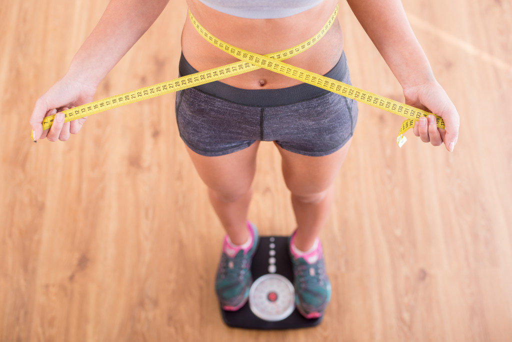 a woman standing on a weighing scale while holding a measuring tape on the waist