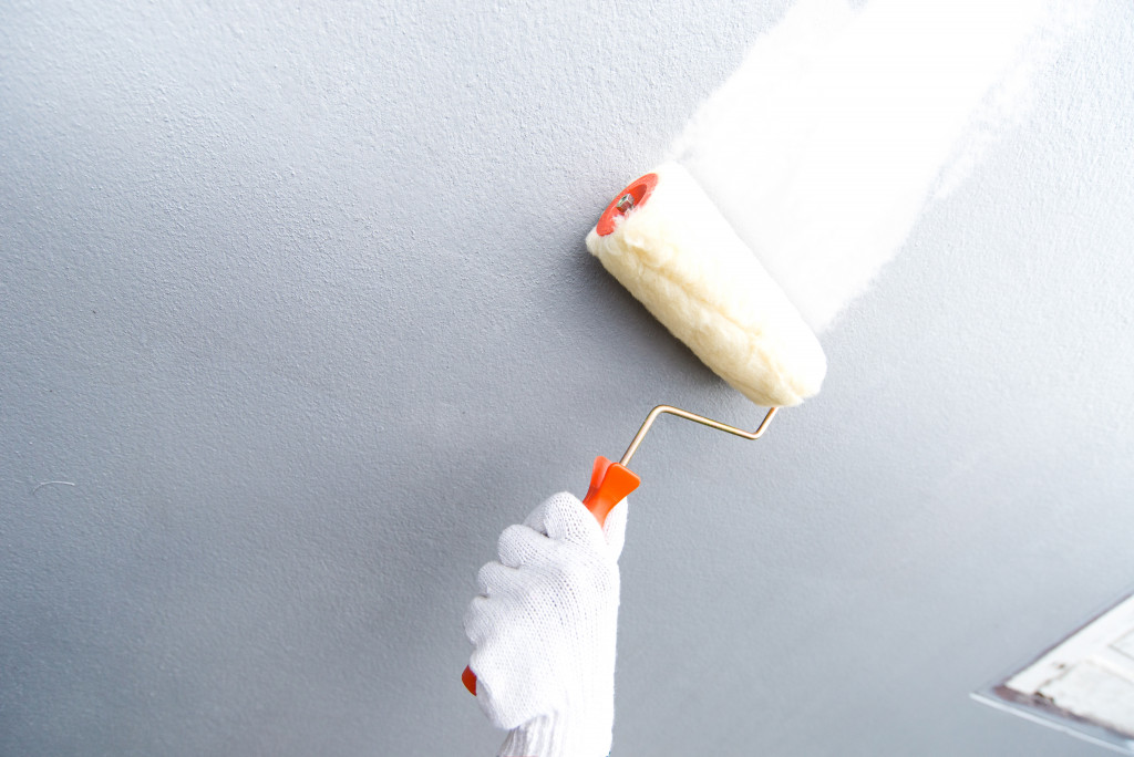 A gloved hand using a paint roller to paint a gray wall white